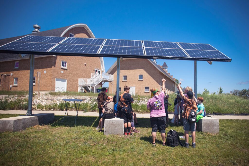 A group of students points upward at the solar panel installation outside Historic Barns Park.