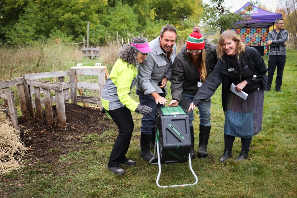 A group of people at the SEEDS farm puts hands together on one of the compost bins at the compost petting zoo.